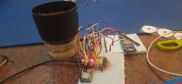 A potted plant beside an ESP32 on a breadboard, wired to a water reservoir